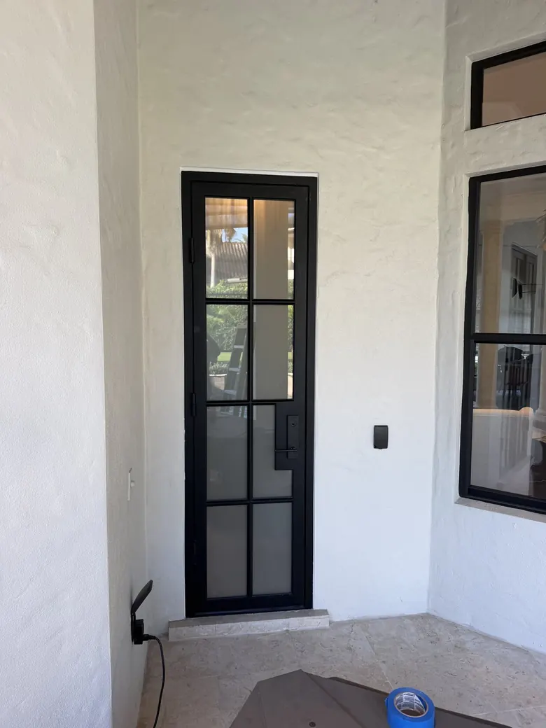 Slim black steel-and-glass single door with divided lites on a white stucco loggia
