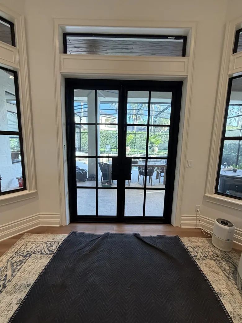 Black steel French double doors with divided-lite glass and transom, interior view to a screened lanai