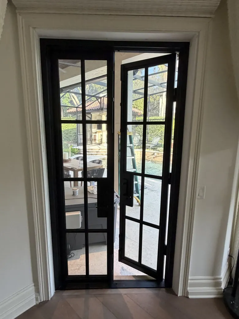 Black steel French doors with one leaf open to the pool terrace