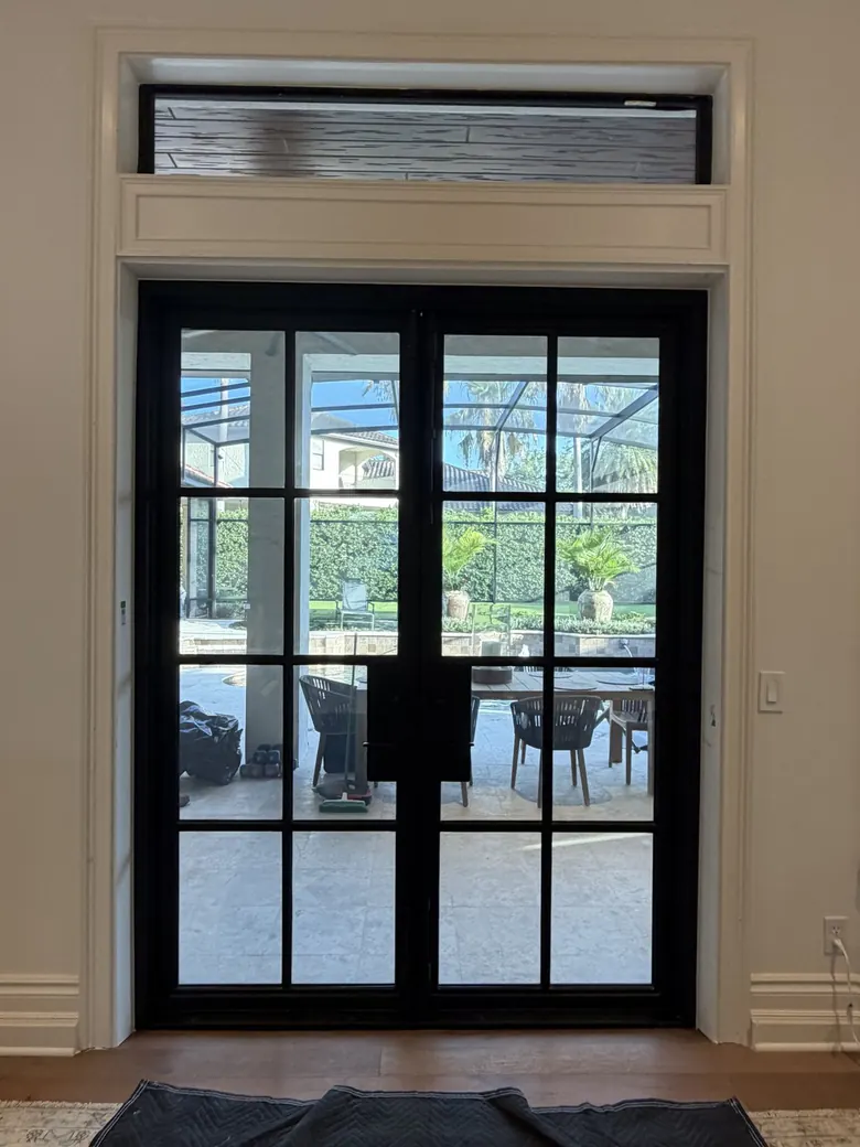 Black steel French double doors with divided lites beneath a transom, straight-on interior view