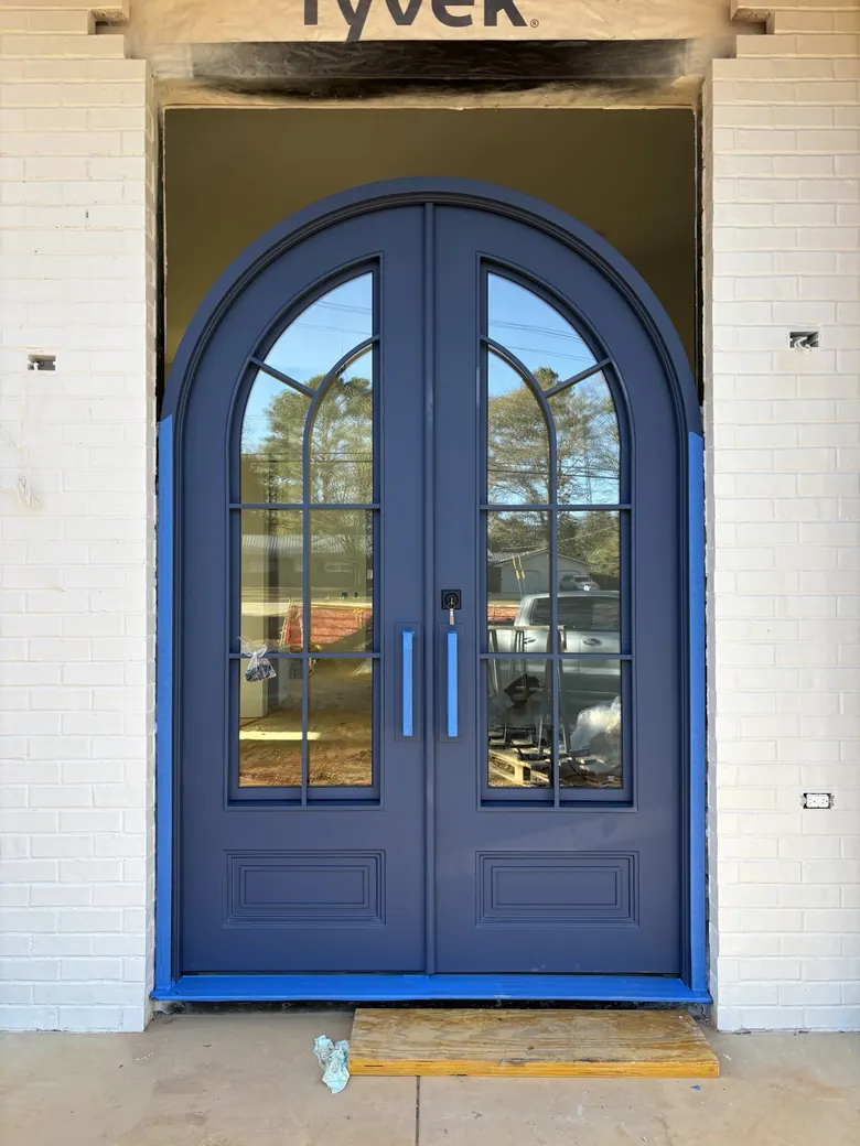 Round-top double doors in a deep blue finish with arched divided lites and raised base panels, mid-install — PDA Doors & More, Florida