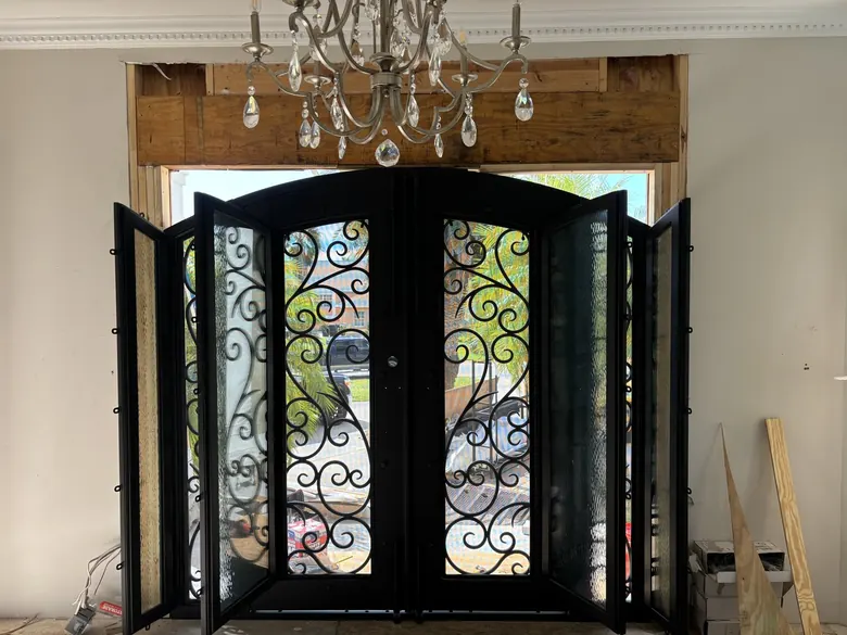 Arched iron door with glass panels swung open during production — ordering and manufacturing coordination